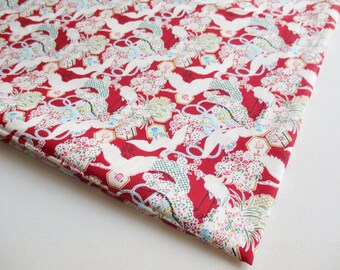 May include: Red fabric with a white crane pattern. The cranes are flying in a circle around a floral design. The fabric has a subtle sheen.