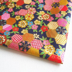 May include: A navy blue fabric with a repeating pattern of pink, red, gold, and white geometric shapes. The shapes are arranged in a hexagonal pattern and are surrounded by small pink, red, and white flowers.