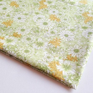 May include: Green fabric with a white floral pattern. The flowers are stylized daisies with yellow centers.