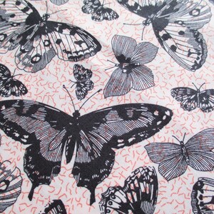 May include: A white fabric with a repeating pattern of black butterflies. The butterflies are in various sizes and positions, creating a dynamic and whimsical design.
