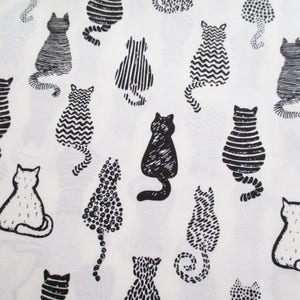 Op de afbeelding: Witte stof met een herhalend patroon van zwarte en witte katten. De katten staan in verschillende poses en hebben verschillende patronen op hun lichaam.