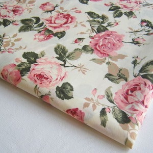 May include: A white fabric with a pink and green floral pattern. The fabric features a repeating pattern of pink roses with green leaves.