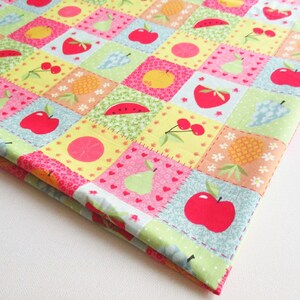 May include: A colourful fabric with a patchwork design featuring various fruits such as apples, pears, pineapples, watermelons, and cherries. The fabric has a yellow background with pink, green, and blue squares.