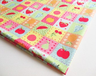 Könnte beinhalten: Ein farbenfroher Stoff mit Patchwork-Muster, das verschiedene Früchte wie Äpfel, Birnen, Ananas, Wassermelonen und Kirschen zeigt. Der Stoff hat einen gelben Hintergrund mit rosa, grünen und blauen Quadraten.