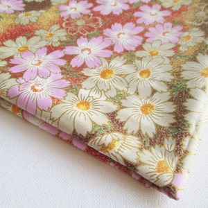 May include: A beige fabric with a floral pattern featuring pink and white flowers on a brown background.