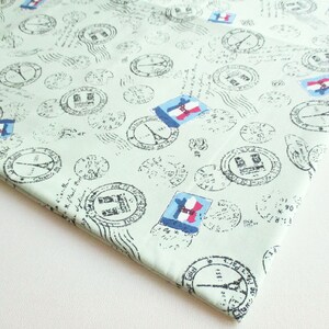 May include: Light green fabric with a repeating pattern of postage stamps and French flag motifs. The stamps feature the Eiffel Tower and other Parisian landmarks. The fabric has a vintage, travel-themed aesthetic.