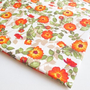May include: White fabric with a repeating pattern of orange flowers with brown centres and green leaves.