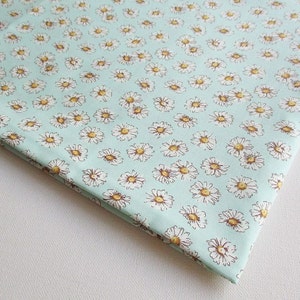 May include: A light blue fabric with a white daisy print. The fabric is folded in the corner.