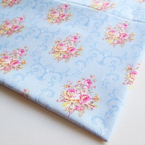 May include: Light blue fabric with a floral pattern of pink and yellow roses on a white background. The fabric has a delicate, vintage feel.