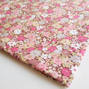 May include: A brown fabric with a pink and white floral print. The fabric is covered in small flowers of various sizes and shapes.