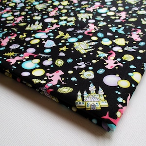 May include: Black fabric with a repeating pattern of mermaids, castles, seashells, stars, fish, and bubbles in pink, yellow, blue, and green.