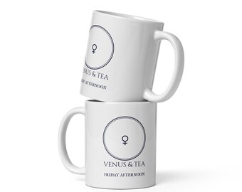 Könnte beinhalten: Zwei weiße Keramikbecher, die vertikal gestapelt sind. Jeder Becher zeigt ein dunkelblaues kreisförmiges Emblem mit einem Venus-Symbol darin, gefolgt von dem Text VENUS & TEA und FRIDAY AFTERNOON, der in einer dunkelblauen Serifenschrift gedruckt ist.