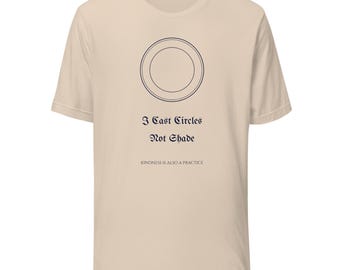 Könnte beinhalten: Ein beiges Kurzarm-T-Shirt mit einer dunkelblauen Grafik aus zwei konzentrischen Kreisen. Unter den Kreisen steht der Text I Cast Circles Not Shade in einer gotischen Schrift, gefolgt von dem kleineren Text KINDNESS IS ALSO A PRACTICE.