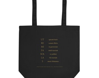 Könnte beinhalten: Eine schwarze Tragetasche mit goldenem Textaufdruck auf der Vorderseite. Der Text zeigt den Liedtext des Hymnus Ut queant laxis in einer vertikalen Liste, wobei die Noten UT, RE, MI, FA, SOL, LA und S links in Gold ausgerichtet sind.