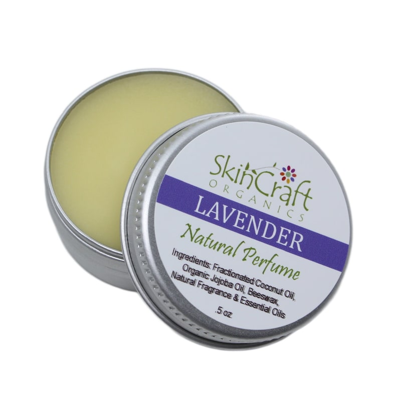 May include: A silver tin with a lavender-colored label that reads "SkinCraft Organics Lavender Natural Perfume". The label also lists the ingredients: Fractionated Coconut Oil, Organic Jojoba Oil, Beeswax, Natural Fragrance & Essential Oils. The tin contains a yellow balm and is labeled with "5 oz".