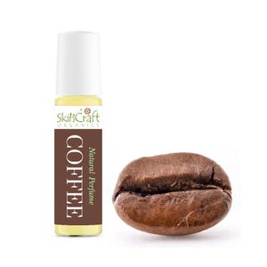 May include: A roll-on perfume bottle labeled "Coffee" with a white cap, next to a single coffee bean. The bottle has a brown label with white text and the words "Natural Perfume". The coffee bean is brown.
