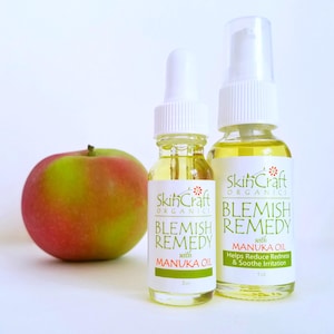 Könnte beinhalten: Zwei Flaschen SkinCraft Organics Blemish Remedy mit Manukaöl. Die kleinere Flasche ist 5 ml und die größere Flasche 30 ml. Die Flaschen sind aus klarem Glas mit weißen Kappen und Etiketten. Die Etiketten sind weiß mit grünem Text und einem grünen Blumenlogo.