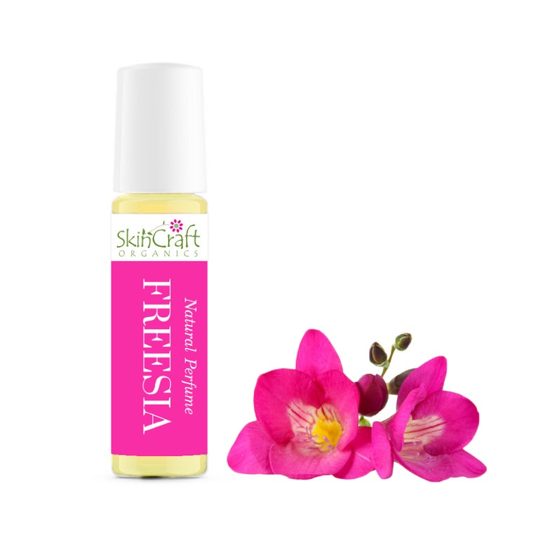 Puede incluir: Un peque&ntilde;o frasco de vidrio de perfume natural de fresia con una tapa blanca de rodillo. El frasco tiene una etiqueta blanca con texto verde que dice "SkinCraft Organics" y "Natural Perfume" sobre la palabra "FREESIA". Una flor de fresia rosa se muestra en el fondo.