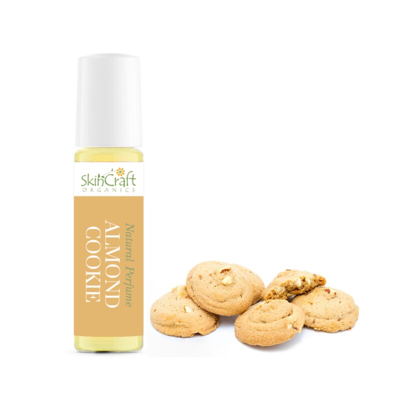 Puede incluir: Un peque&ntilde;o frasco de vidrio de perfume natural con aroma a almendra y galleta. El frasco tiene una tapa blanca de rodillo y una etiqueta amarilla con el texto "SkinCraft Organics" y "Natural Perfume Almond Cookie". Hay cinco galletas de almendras en el fondo.