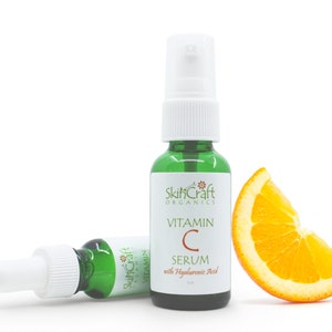 Könnte beinhalten: Zwei grüne Glasflaschen mit SkinCraft Organics Vitamin C Serum mit Hyaluronsäure. Die Flasche rechts hat einen weißen Pumpspender. Die Flasche links hat einen weißen Tropfer. Eine Orangenscheibe befindet sich im Vordergrund.