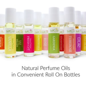 Pu&ograve; includere: Una collezione di flaconi di profumo roll-on con tappi bianchi. Ogni flacone ha un'etichetta con un nome di fragranza diverso, tra cui "Vaniglia", "Rosa" e "Tuberosa". Il testo "Natural Perfume Oils in Convenient Roll On Bottles" &egrave; visualizzato sotto.