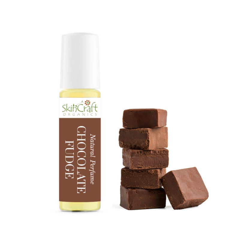 Puede incluir: Una botella de vidrio de Perfume Natural SkinCraft Organics Chocolate Fudge. La botella es amarilla y tiene una tapa blanca. En el fondo, hay varios trozos de fudge de chocolate apilados uno encima del otro.