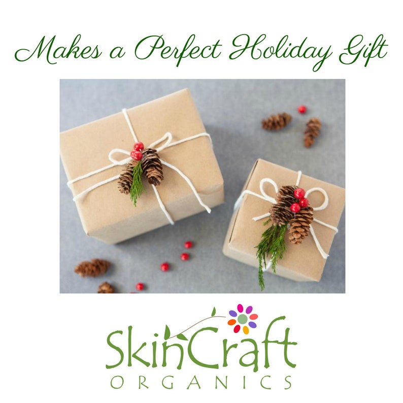 May include: Two brown gift boxes wrapped with twine and decorated with pine cones and red berries. The boxes are on a gray background. The text "Makes a Perfect Holiday Gift" is above the boxes. The text "SkinCraft Organics" is below the boxes.