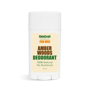 Op de afbeelding: Een witte deodorantstick met een label met de tekst "SkinCraft Organics FOR MEN AMBER WOODS DEODORANT 100% Natural No Aluminum 2.5 oz". Het label is beige met oranje en groene tekst.