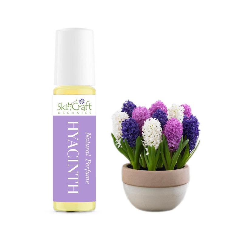 May include: A glass bottle of SkinCraft Organics Natural Perfume in Hyacinth. The bottle has a white label with purple text. A bouquet of purple, white, and blue hyacinths in a light brown pot is in the background.