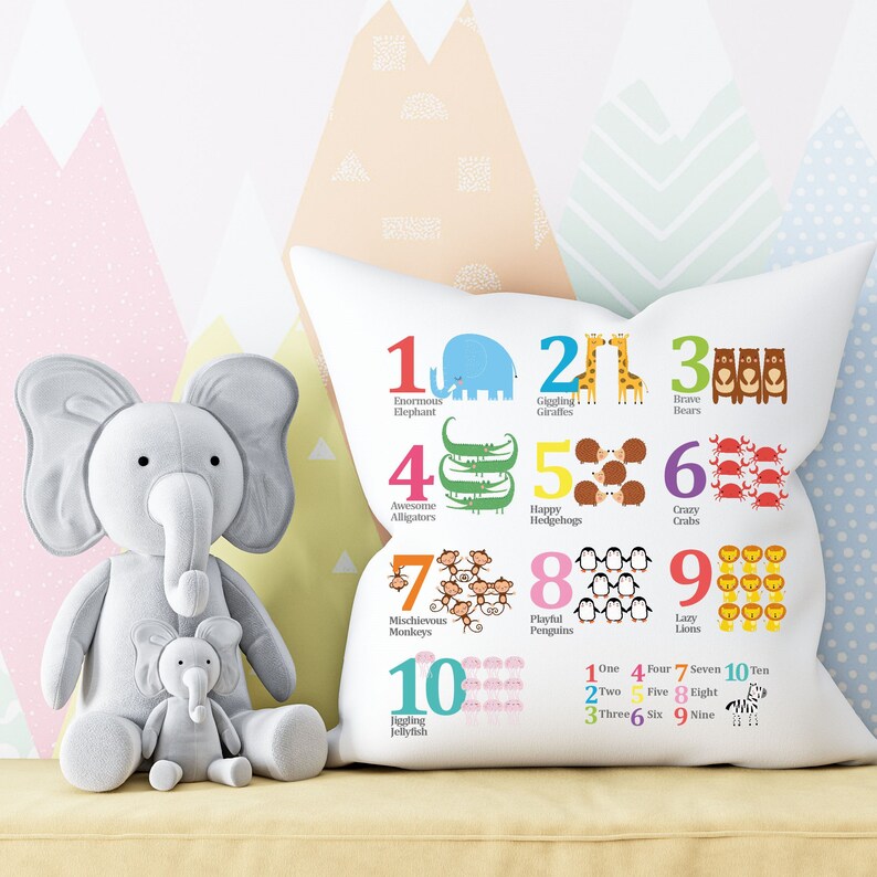 K&ouml;nnte beinhalten: Ein wei&szlig;es Kissen mit bunten Zahlen und Tierillustrationen. Die Zahlen reichen von 1 bis 10, und jede Zahl ist mit einem Tier gepaart. Die Tiere sind ein Elefant, eine Giraffe, ein B&auml;r, ein Alligator, ein Igel, eine Krabbe, ein Affe, ein Pinguin, ein L&ouml;we und eine Qualle. Das Kissen hat auch die Zahlen von eins bis zehn unter den Illustrationen ausgeschrieben.