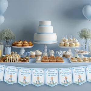 K&ouml;nnte beinhalten: Ein Tisch mit einer dreist&ouml;ckigen wei&szlig;en Torte, Cupcakes und Geb&auml;ck. Das Banner lautet "Harry's Christening". Die Desserts sind auf wei&szlig;en Servierplatten mit blauen Akzenten angerichtet.