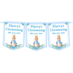 K&ouml;nnte beinhalten: Eine hellblaue Girlande mit dem Text "Harry's Christening 28th June 2026", der dreimal wiederholt wird. Jede Girlande zeigt eine Aquarellillustration eines Kaninchens mit blauem Jackett und blauen Blumen.