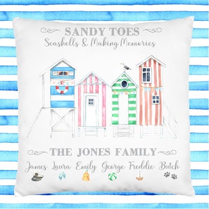 May include: White cushion with a watercolour illustration of colourful beach huts and the text "SANDY TOES Seashells & Making Memories THE JONES FAMILY James Laura Emily George Freddie Butch".