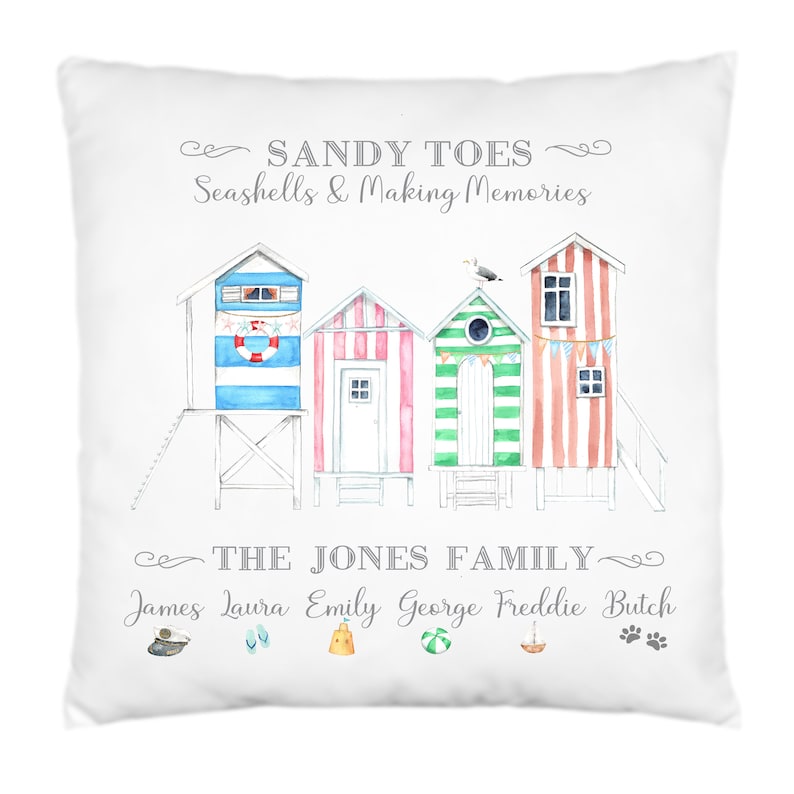 May include: A white cushion with a watercolour illustration of colourful beach huts and the text "SANDY TOES Seashells & Making Memories THE JONES FAMILY James Laura Emily George Freddie Butch".