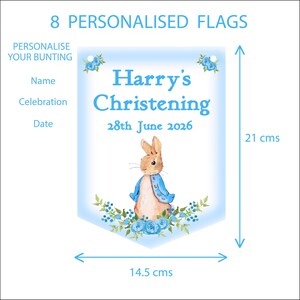 K&ouml;nnte beinhalten: Eine personalisierte Flagge f&uuml;r eine Taufe mit dem Text "Harry's Christening" und dem Datum "28. Juni 2026". Die Flagge ist 14,5 cm breit und 21 cm hoch, mit einer Peter-Rabbit-Illustration und floralen Akzenten. Der Text "8 personalisierte Flaggen" steht oben.