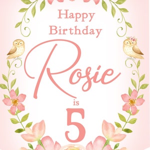 Op de afbeelding: Een roze en groene bloemen-verjaardagsbord met de tekst "Happy Birthday Rosie is 5". Twee uilen zitten op takken aan weerszijden van de tekst.