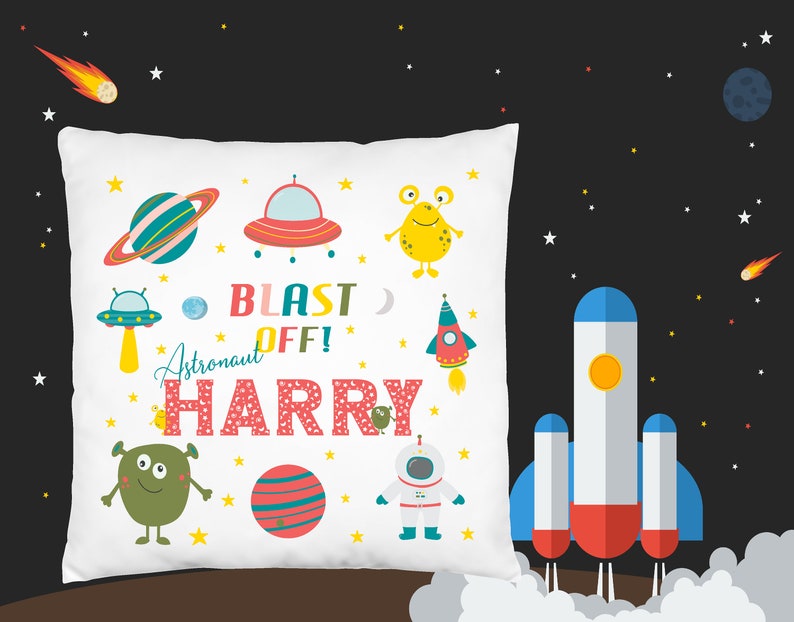 K&ouml;nnte beinhalten: Wei&szlig;es Kissen mit einem Weltraum-Motiv. Es zeigt eine Rakete, Planeten, Au&szlig;erirdische und den Text "Blast Off! Astronaut Harry".