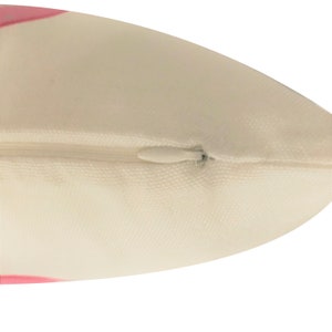 May include: Close-up of a white pillow with a pink trim and a zipper closure.