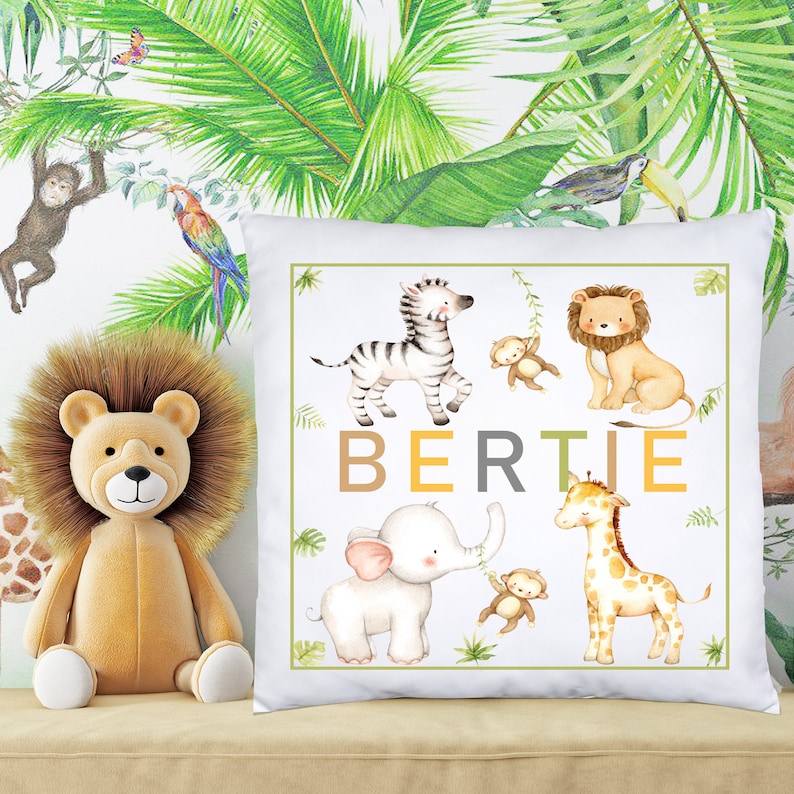 K&ouml;nnte beinhalten: Ein wei&szlig;es Kissen mit Dschungeltier-Motiv. Das Kissen zeigt ein Zebra, einen L&ouml;wen, einen Elefanten, eine Giraffe und Affen. Der Name "BERTIE" ist in braunen, gelben und grauen Buchstaben geschrieben.