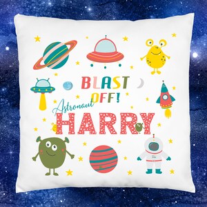 K&ouml;nnte beinhalten: Wei&szlig;er Kissenbezug mit Weltraumthema. Er zeigt eine Rakete, Planeten, Sterne, Au&szlig;erirdische und ein Raumschiff. Der Text lautet "Blast Off! Astronaut Harry".