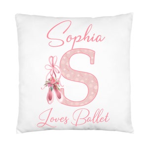 K&ouml;nnte beinhalten: Ein wei&szlig;es Kissen mit rosa Schriftzug "Sophia S loves Ballet". Das S ist mit einem rosa Blumenmuster und einem Paar rosa Ballettschuhen mit einer rosa Schleife verziert.
