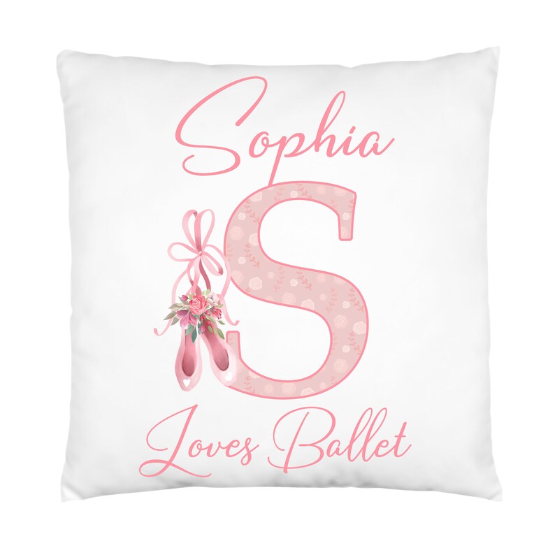 K&ouml;nnte beinhalten: Ein wei&szlig;es Kissen mit rosa Schriftzug "Sophia S loves Ballet". Das S ist mit einem rosa Blumenmuster und einem Paar rosa Ballettschuhen mit einer rosa Schleife verziert.
