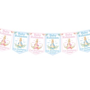 May include: A baby shower banner with eight pink and blue pennants. Each pennant features a Peter Rabbit illustration and the text "Baby Robinson" and "Can Anybunny Guess?"