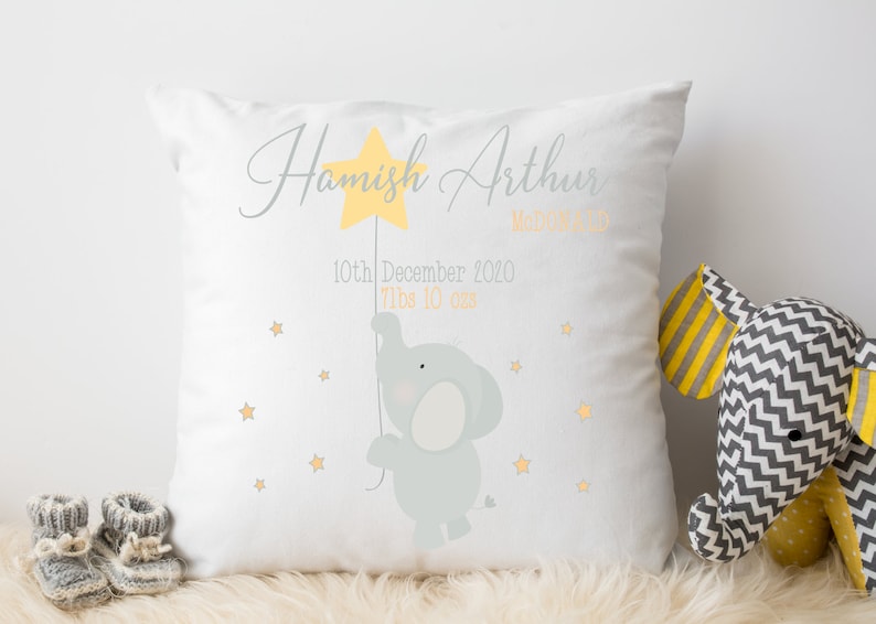 May include: A white pillow with a gray elephant holding a yellow star. The pillow is personalized with the name "Hamish Arthur" and the date "10th December 2020".