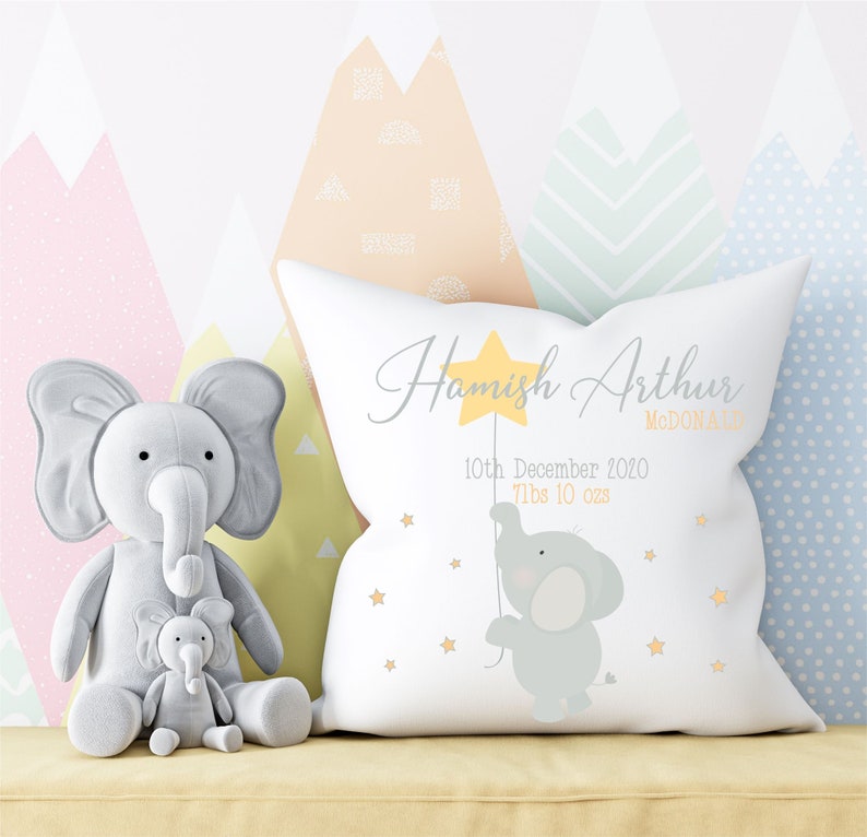 May include: White pillow with a gray elephant holding a yellow star. The pillow is decorated with yellow stars and the text "Hamish Arthur McDonald, 10th December 2020, 7lbs 10 ozs".