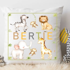 K&ouml;nnte beinhalten: Ein wei&szlig;es Kissen mit gr&uuml;nem Rand, auf dem ein Zebra, ein L&ouml;we, ein Elefant und eine Giraffe mit dem Namen "BERTIE" in braunen, gelben und grauen Buchstaben abgebildet sind.