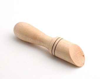 May include: A light-colored wooden muddler with a rounded handle and a flat, angled end. Two dark lines encircle the base of the muddler's head. The kitchen tool is designed for mixing ingredients in a glass.