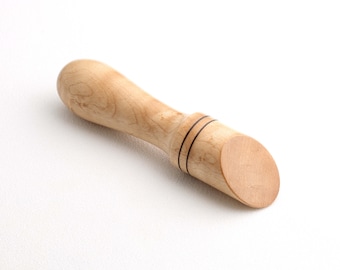 May include: A wooden spoon with a rounded handle and a flat, slightly curved head. The spoon is made of light wood with dark brown accents.