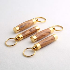 Peut inclure: Trois porte-clés en bois avec des anneaux et des capuchons en métal doré. Les porte-clés sont en bois d'olivier avec un motif de grain de bois naturel.