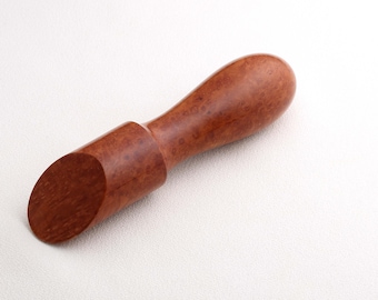 May include: A wooden scoop with a handle and a slanted scoop end. The scoop is made of a reddish-brown wood with a natural grain pattern. The handle is rounded and smooth, and the scoop end is angled for easy use.